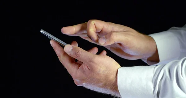 Close - up of male hands in white shirt electronic gadget phone with touch screen scrolling and tapping on black isolated background. Mobile device for Internet access