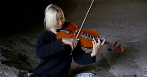 female violinist is playing concert in natural cave in daytime, unusual place