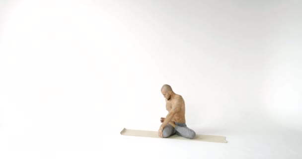 Bald athlete is sitting on sporty mat and spinning torso, stretching muscles of back, legs and hands, warming body — Stock Footage Bald athlete is sitting on sporty mat and spinning torso, stretching muscles of back, legs and hands, warming body Royalty Free Stock Video