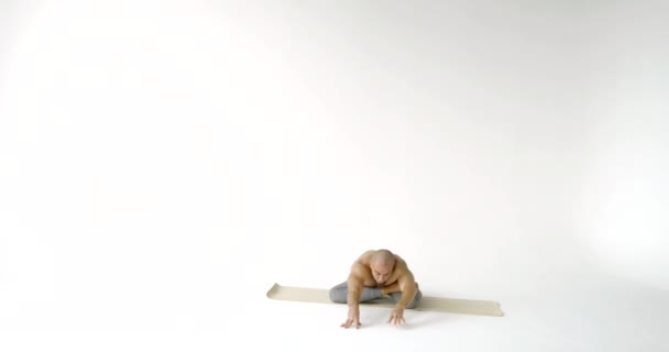 Muscular man does difficult yoga asana sitting in full split and bending on mat in large white studio slow motion — Stock Footage Muscular man does difficult yoga asana sitting in full split and bending on mat in large white studio slow motion Royalty Free Stock Video