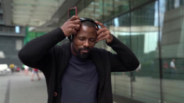 Ein afroamerikanischer Geschäftsmann mit kabellosen Kopfhörern in der Nähe eines Bürogebäudes. Business, Menschen, Musik, Technologie, Freizeit- und Lifestylekonzepte.