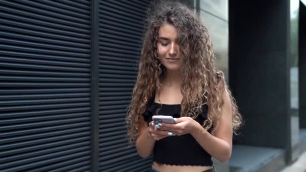 a beautiful girl with curly hair walks around the city with a mobile phone to access social networks