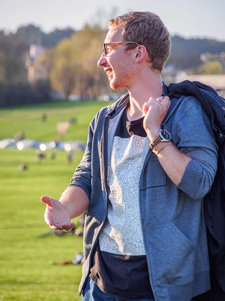 Side view of a laughing blonde white young man in glasses  (on a background of a city park)