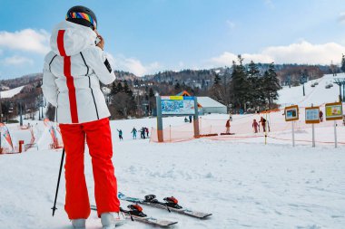 Hokkaido, Japonya - Aralık 2019: Kayak alanında kar geçmişine sahip ekipmanlı kayakçı kız. Kış mevsiminde kar kayakları Kiroro kayak merkezinin en tepesindeki dağlarda.