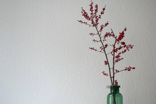 Beyaz duvar arka plan üzerinde winterberry dalları ile yeşil vazo