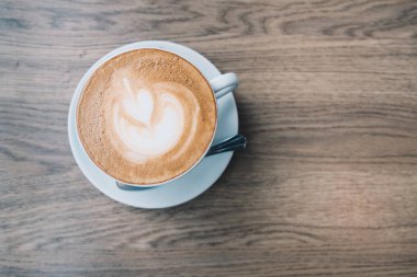 Ahşap masa arka plan üzerinde latte sanat ile beyaz bir fincan sıcak kahve Latte üstten görünüm.