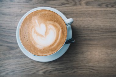Ahşap masa arka plan üzerinde latte sanat ile beyaz bir fincan sıcak kahve Latte üstten görünüm.