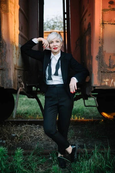 blonde woman in the classic suit standing between carriages and looking at the camera