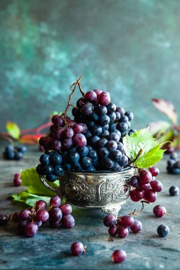 Rustik bir arka plan üzerinde metal bir kase içinde üzüm yaprakları ile kırmızı ve siyah üzüm. Kopya alanı.