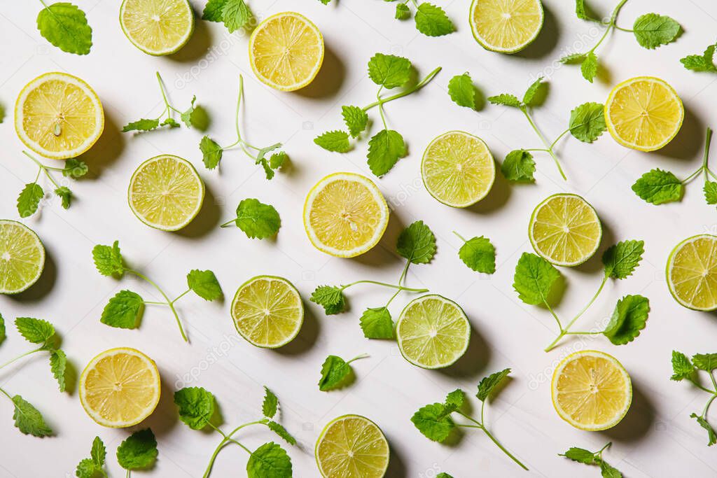 Colorful citrus fruit halves and green leaves on white marble background. Lemon and lime. Flat lay, top view.