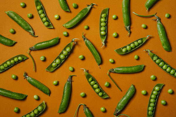 Top view of fresh green pea pods and peas on orange background. Creative food concept. Flat lay.