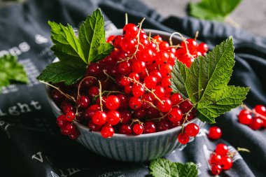 Gri bir mutfak havlusunda gri bir seramik kasede yaprakları olan kırmızı frenk üzümü. Kapat..