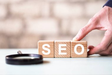 Arama motoru optimizasyonu web konsepti. Kelime seosu ve büyüteçle ahşap blok şekline el koyuyorum.