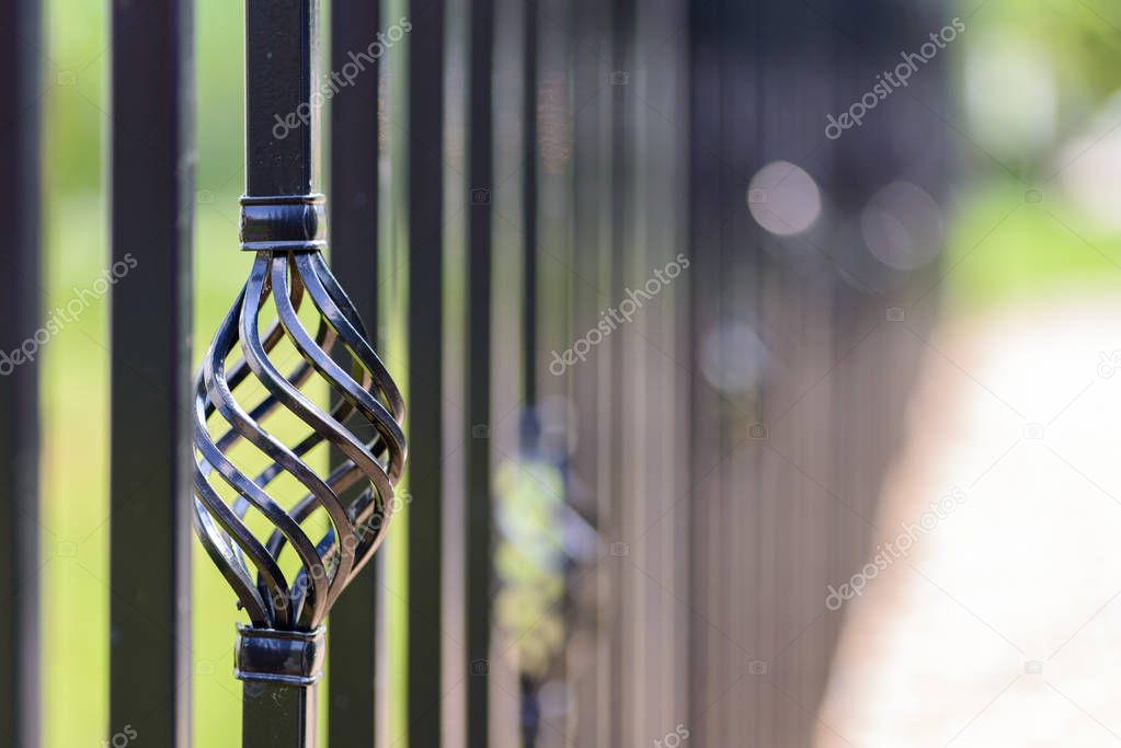 Black decorative metal fence, angular iron rods and curved upper part. Close-up of the decoration on the side.
