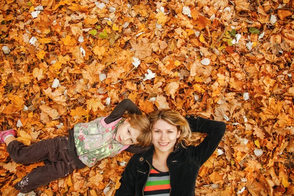 Donna felice con un bambino sulle foglie autunnali nella natura — Foto Stock