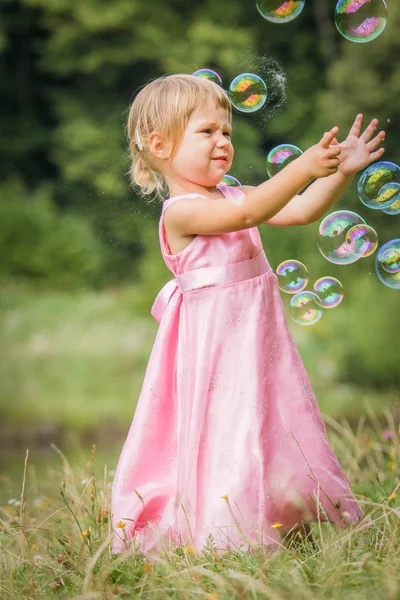 Happy little girl chasing bubbles on nature in the park — Stock Photo, Image