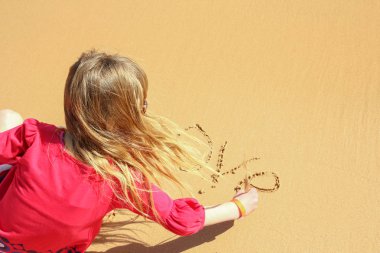 Mutlu çocuk deniz arka plan yakınındaki kum üzerinde çizer