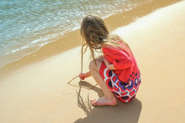 Glückliches Kind zeichnet auf den Sand in der Nähe des Meereshintergrunds — Stockfoto