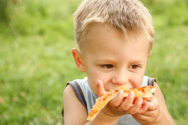 Criança comendo uma pizza saborosa sobre a natureza da grama no par — Fotografia de Stock