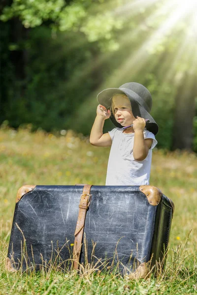 Lycklig Baby flicka med en resväska utomhus i parken — Stockfoto