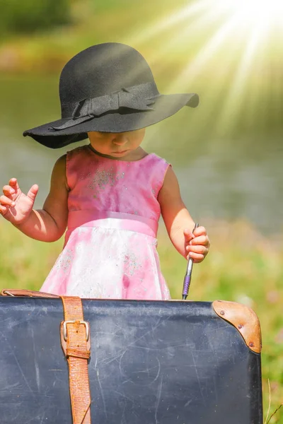 Lycklig Baby flicka med en resväska utomhus i parken — Stockfoto