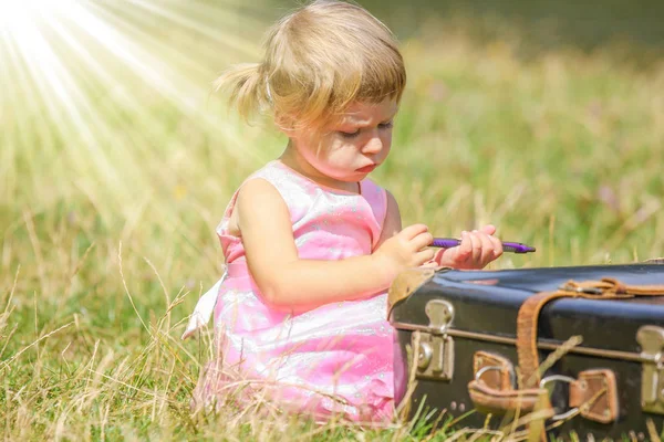 Happy baby girl with a suitcase outdoors at the park — Stock Photo, Image