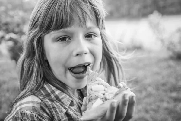 Niño comiendo una sabrosa pizza en la naturaleza de la hierba a la par —  Fotos de Stock