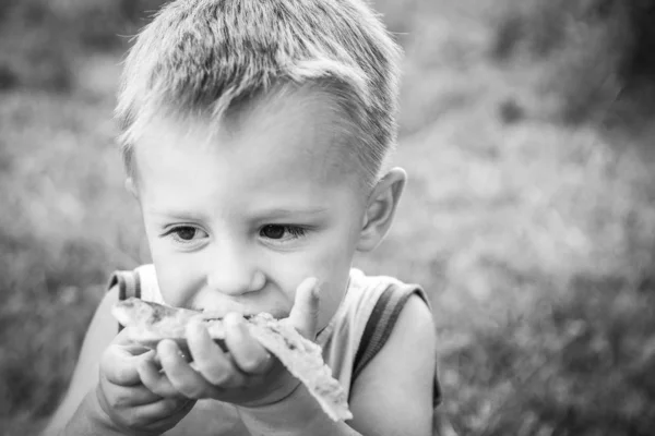 Ребенок ест вкусную пиццу о природе травы в пар — стоковое фото