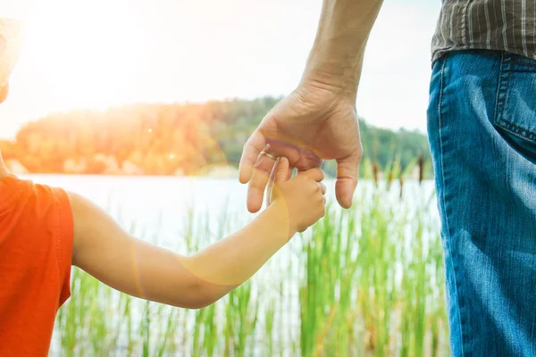 Händerna på en förälder och barn i naturen i en park vid havet — Stockfoto