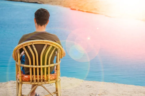 Счастливый парень, сидящий на табуретке на фоне моря на природе — стоковое фото