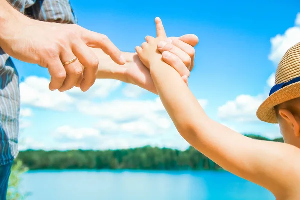 Händerna på en förälder och barn i naturen i en park vid havet — Stockfoto
