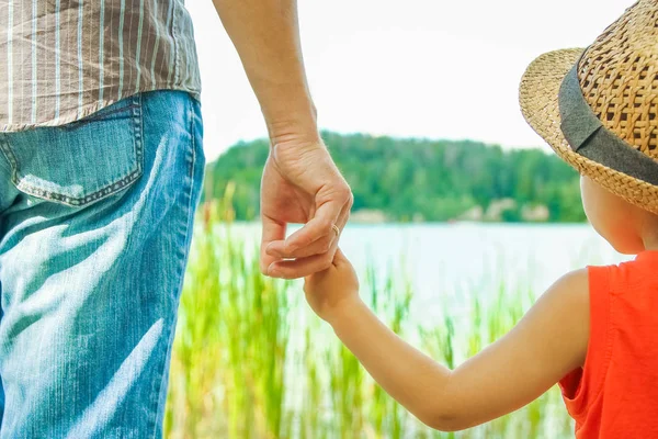 Manos de un padre y un niño en la naturaleza en un parque junto al mar — Foto de Stock