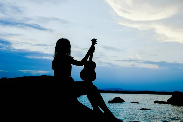 Happy girl with ukulele by the sea on nature silhouette backgrou — Stock Photo, Image