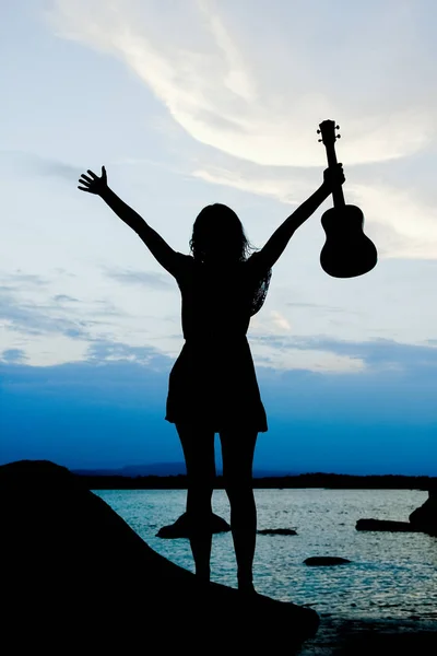 Chica feliz con ukelele por el mar en la silueta de la naturaleza backgrou —  Fotos de Stock