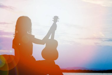 Doğa üzerinde deniz tarafından ukulele ile mutlu kız siluet backgrou