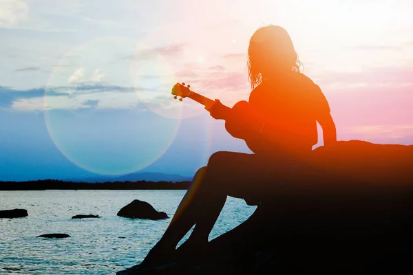 Gelukkig meisje met ukulele door de zee op natuur silhouet backgrou — Stockfoto