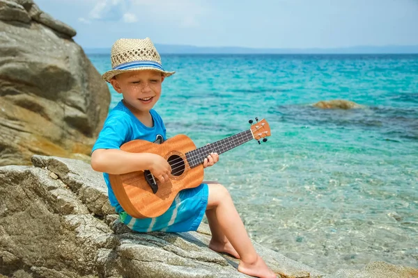 Szczęśliwy dziecko gra na gitarze przez morze Grecja na Nature oświetlenie tła — Zdjęcie stockowe