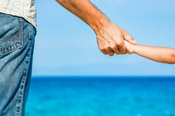 Mutlu baba, Yunan Denizi kıyısında bir çocuğun elini tutuyor. — Stok fotoğraf