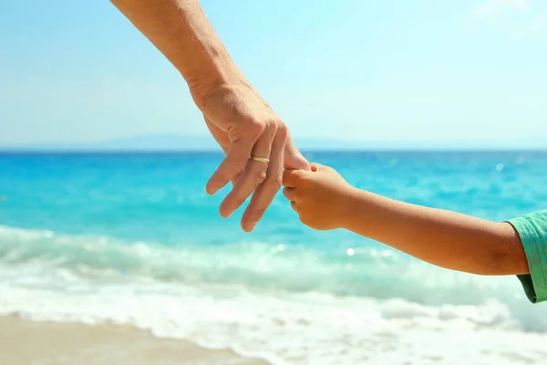 Händerna på förälder och barn vid havet på stranden — Stockfoto
