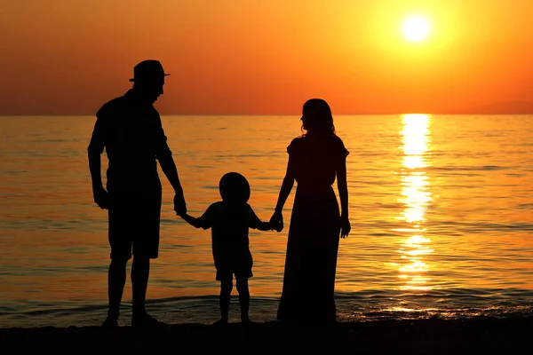 Familjens silhuett vid solnedgången vid havet... — Stockfoto