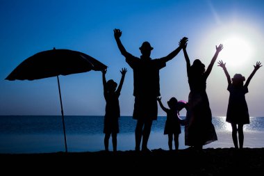 Gün batımında deniz kenarında mutlu bir aile doğada gezici bir siluette