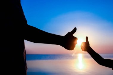 Mutlu baba ve çocuğun elleri deniz kenarında, doğanın siluetinde.