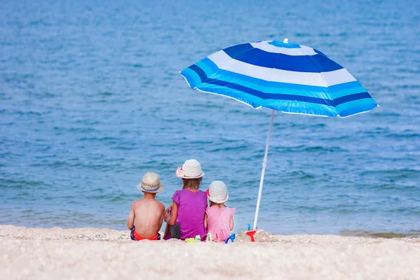 傘を背に海で遊ぶ幸せな子供たち — ストック写真