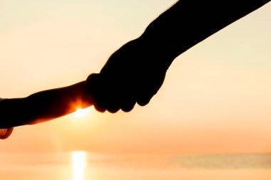 Mutlu baba ve çocuğun elleri deniz kenarında, doğanın siluetinde.