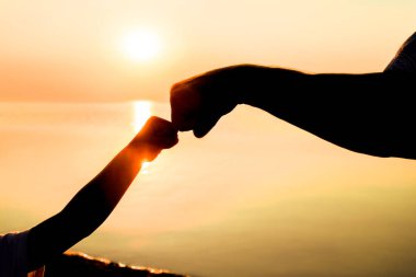 Mutlu baba ve çocuğun elleri deniz kenarında, doğanın siluetinde.