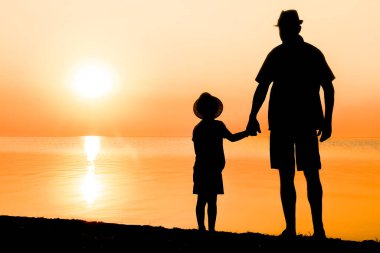 Deniz kenarında çocuklu mutlu bir ebeveyn doğanın silueti üzerinde oynuyor.