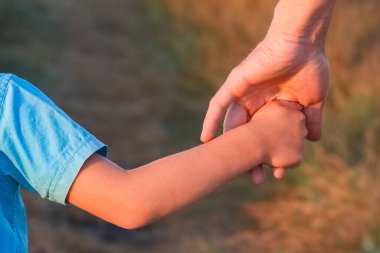 Yolun kenarındaki parkta mutlu bir çocuk ve ebeveynin elleri.