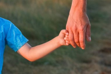Yolun kenarındaki parkta mutlu bir çocuk ve ebeveynin elleri.