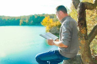 Parkta doğa yolculuğu eğitimi üzerine kitap okuyan mutlu bir adam.