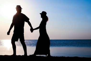 Gün batımında deniz kenarında mutlu bir çift doğada gezici bir siluette